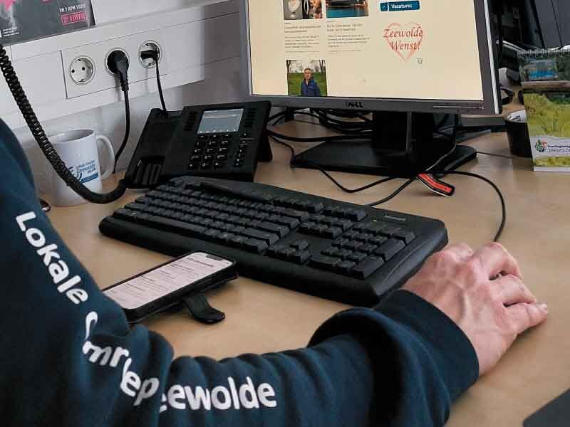 Foto van redacteur bij computer en telefoon, je ziet alleen rechterarm