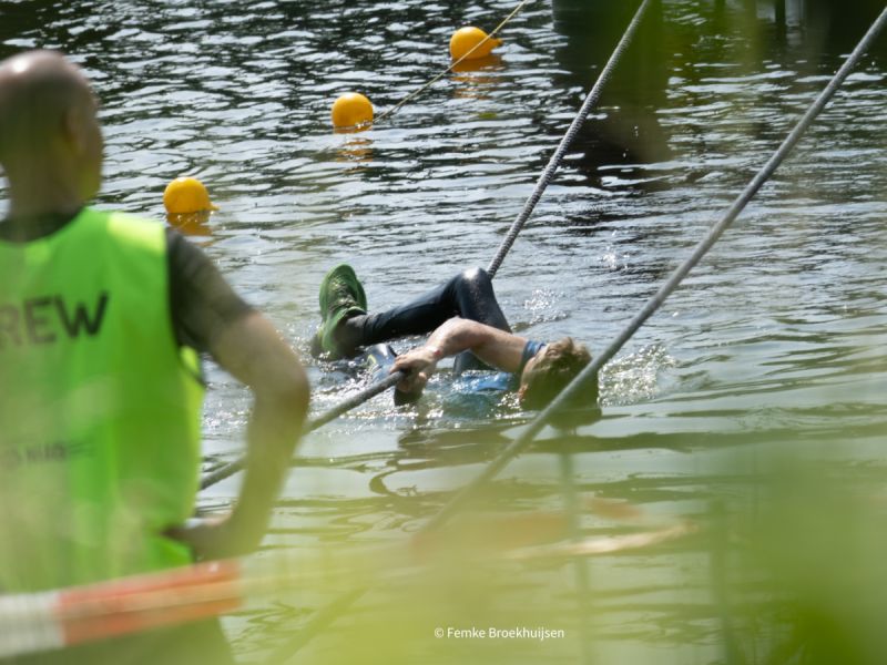 deelnemer survivalrun hangend aan touw boven water